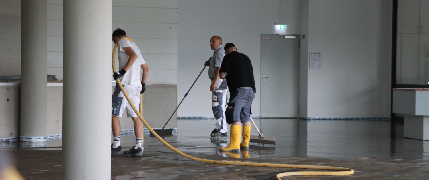 Bodenleger-Team beim Verteilen der Bodenausgleichsmasse in einer großen Gewerbefläche