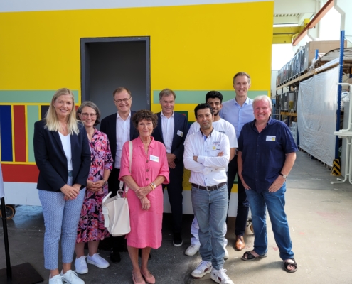 Gruppenbild in der Temps-Ausbildungshalle mit Daniel Terzenbach, Johannes Pfeiffer, deren Begleitung und dem temps-team vor einer bunten Wand