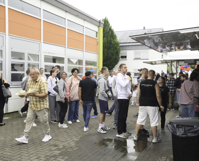 Die hungrigen Mitarbeitenden auf dem Sommerfest stellen sich auf dem Mitarbeiterfest an den Catering-Ständen an. Es gibt Burger und Kuchen zur Auswahl.