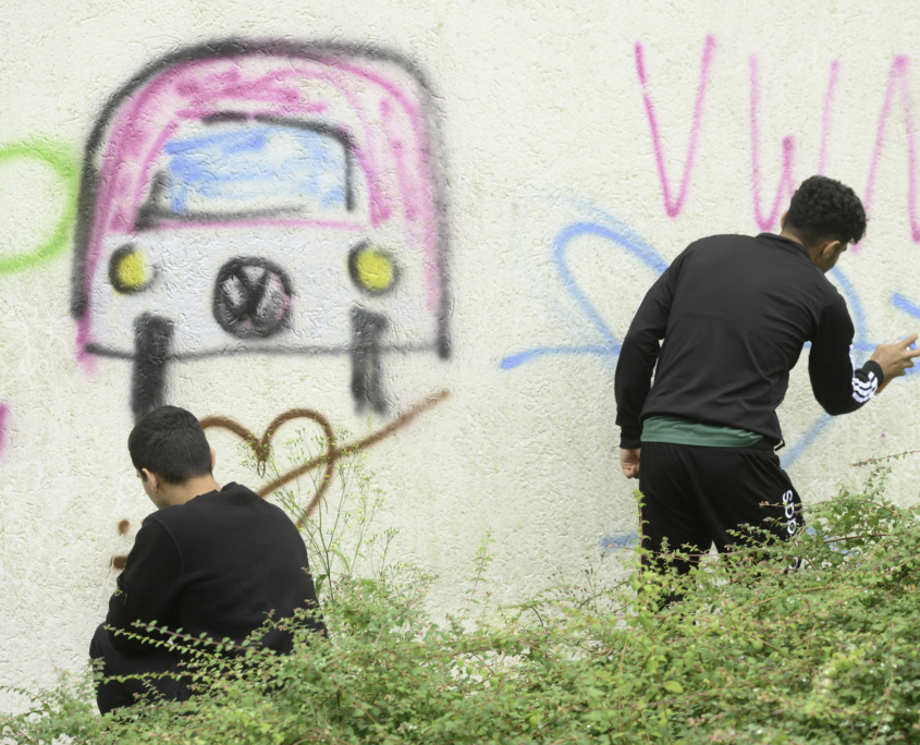 Zwei Teenager sprühen Graffiti-Farbe auf eine weiße Hauswand auf einem Sommerfest