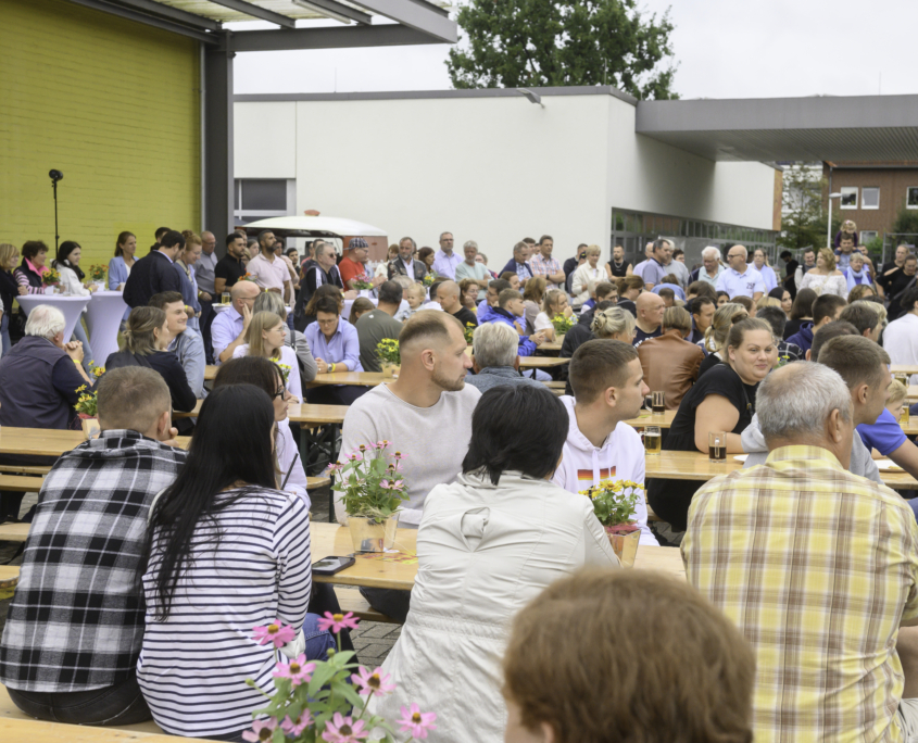 Mitarbeitende auf einem Sommerfest blicken in Richtung Bühne, wo gerade die Eröffnungsrede gehalten wird