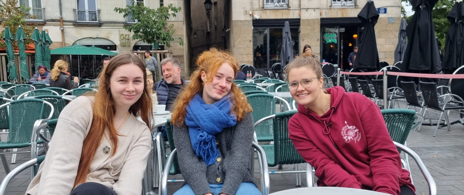 Johanna sitzt im Rahmen ihrer internationalen Ausbildung mit ihren Freundinnen in einem französischen Cafe