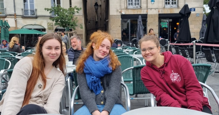 Johanna sitzt im Rahmen ihrer internationalen Ausbildung mit ihren Freundinnen in einem französischen Cafe