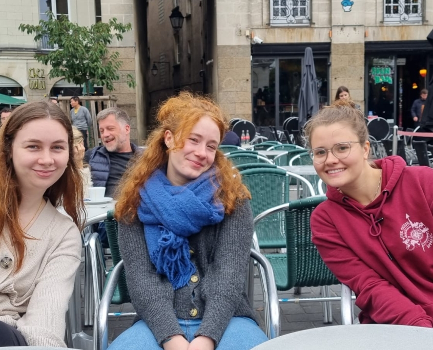 Johanna sitzt im Rahmen ihrer internationalen Ausbildung mit ihren Freundinnen in einem französischen Cafe