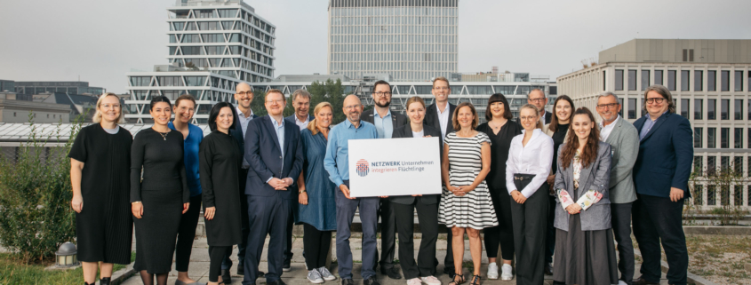 Gruppenfotos des aktuellen Regionalbotschafterjahrgangs vor dem Bundesministerium für Wirtschaft und Klimaschutz. Die Gruppe hält ein Schild mit dem Netzwerknamen "NETZWERK Unternehmen integrieren Flüchtlinge" in die Kamera