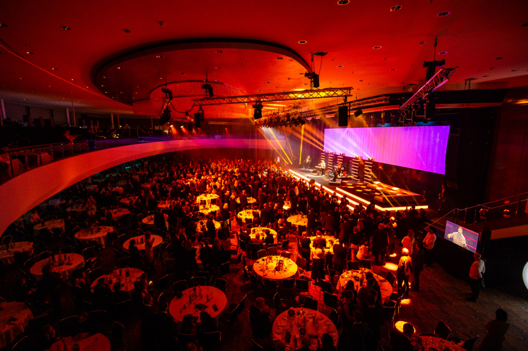 Top-Shot der Abendgala des Deutschen Nachhaltigkeitspreises 2024 im Düsseldorfer Maritim-Hotel mit eingedeckten Tischen und roter Lichtstimmung - Ein Abend voller Nachhaltigkeit